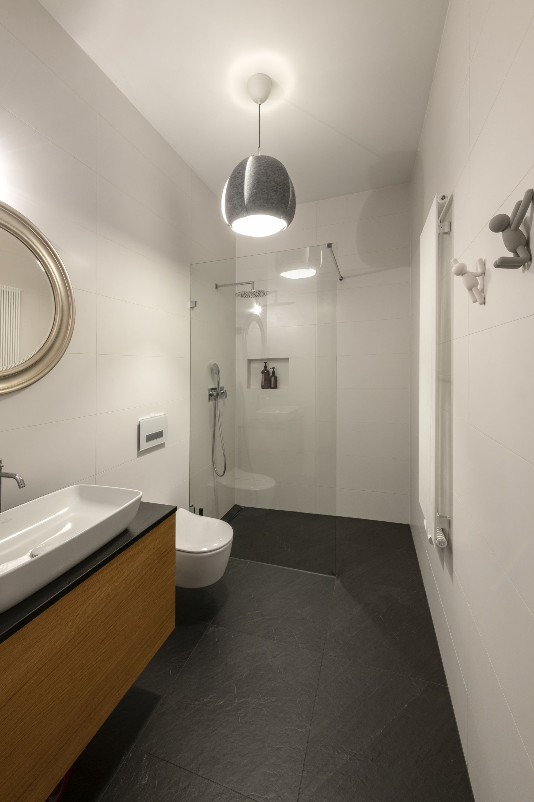 Elegancka łazienka z dużą kabiną prysznicową walk-in, umywalką nablatową na drewnianej szafce i okrągłym lustrem, wyposażona w podgrzewany wieszak na ręczniki.